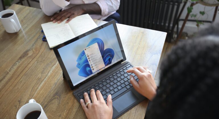 Overhead view of two people at a table working with a Microsoft laptop and notebook