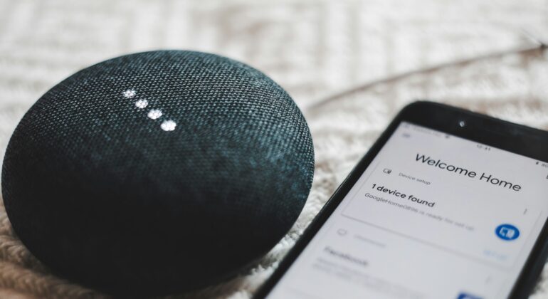 turned-on charcoal Google Home Mini and smartphone