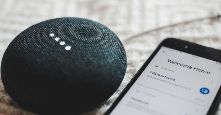 turned-on charcoal Google Home Mini and smartphone