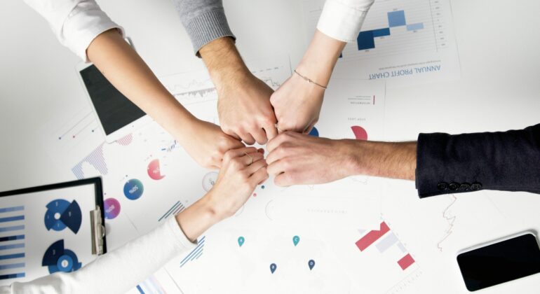 Free Colleagues celebrate success with a fist bump over financial charts depicting teamwork and unity. Stock Photo